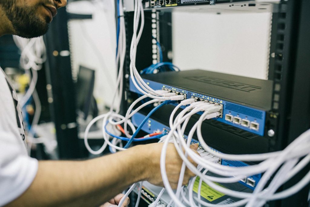 12 Grand Ideas to Supercharge Your Science and Technology News Outputs in Publication, Press Competitions 5 An IT professional configuring network cables in a server rack, focusing on Ethernet connections.