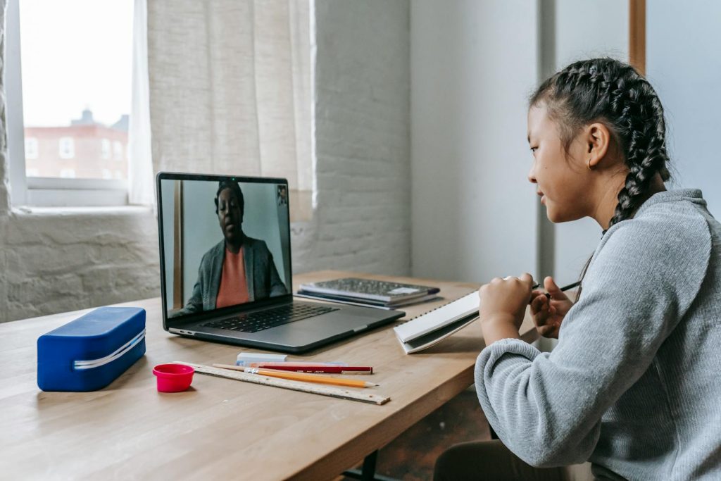 Most Effective, Widely Adopted: Blended Learning is the Ultimate Combo for School Experience Extraordinaire 6 A young girl engages in online education with a teacher via video call, focusing attentively.