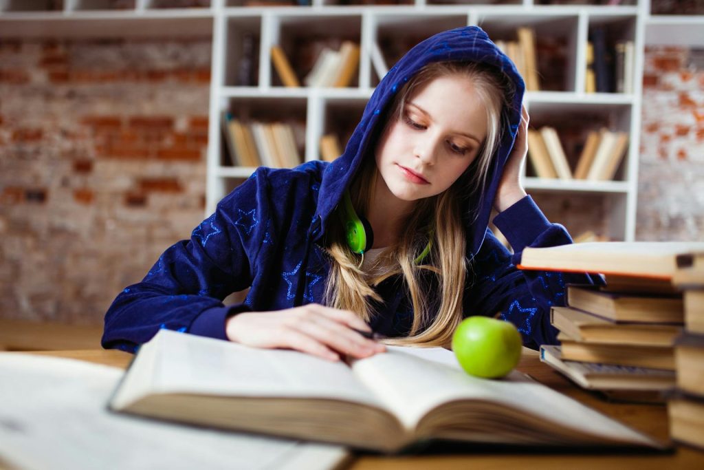 6 Completely Earnest Reasons to Utilize Single-Tasking for More Effective and High-quality Academic Performance 7 Teenage girl in blue hood reads in library, headphones and apple by her side.
