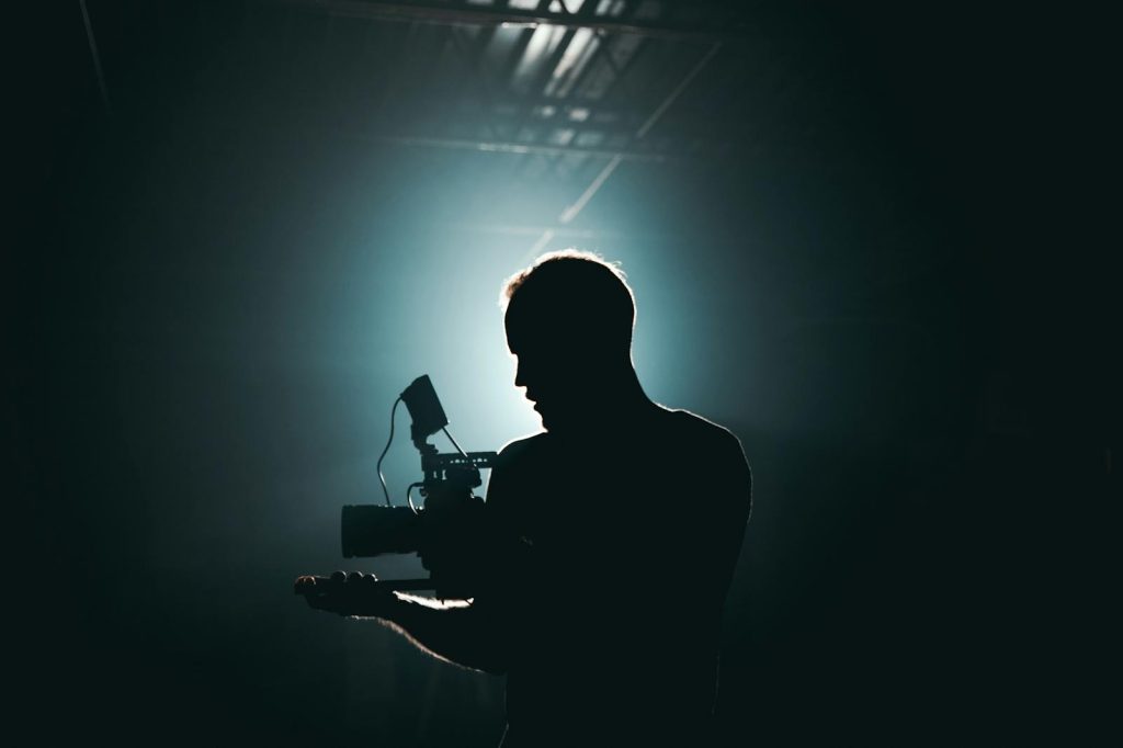 Silhouette of a cinematographer with camera gear in a dramatic, low light setting.