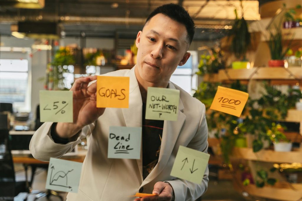 Young man brainstorming with sticky notes on glass wall in modern office setting.